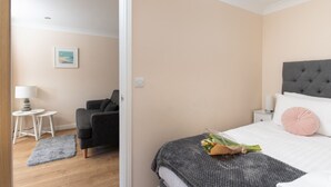 Une chambre à coucher avec un lit, une chaise, une petite table avec une lampe et un tableau au mur.