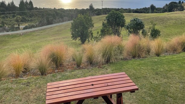 A picnic table in a grassy field with a view of a lake and mountains in the background.
