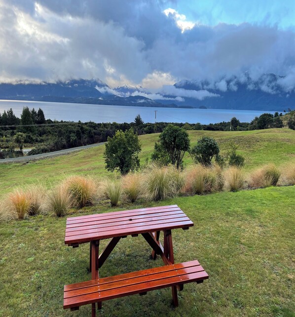 A picnic table in a grassy field with a lake and mountains in the background.
