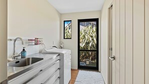 Une cuisine compacte comprenant un évier, un plan de travail et donnant sur un jardin grâce à une porte vitrée.