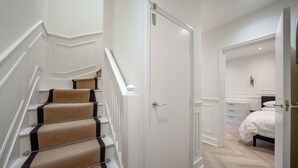 A staircase with beige and black carpeted steps, a white door, and a bedroom with a bed and dresser. - Pimlico Brand New Luxury Home (London)