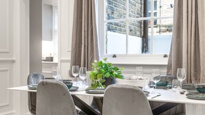 A dining area with a table set for four, a potted plant, and a view of a brick building outside. - Pimlico Brand New Luxury Home (London)