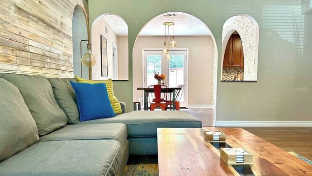 A modern living room with a sectional sofa, a wooden coffee table, and a dining area with a red chair. - Ultimate Furnished Rental-Centrally Located (Aurora)