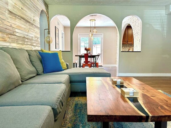 A modern living room with a sectional sofa, a wooden coffee table, and a dining area with a red chair.