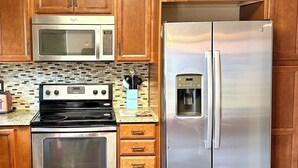A kitchen with wooden cabinets, a stainless steel microwave, a double oven, a refrigerator, and a water dispenser. - Ultimate Furnished Rental-Centrally Located (Aurora)