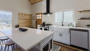 Une cuisine moderne avec des meubles blancs, un grand îlot central, un four encastré et une vue sur les montagnes.