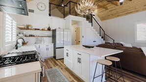 Une cuisine moderne avec des meubles blancs, un îlot central et un coin repas agrémenté d’un canapé en cuir marron.