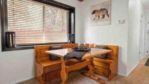 Ein Essbereich mit einem Holztisch und gepolsterten Bänken, sowie einem Fenster mit Jalousien.