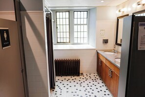 A bathroom with a tiled floor, a window, a radiator, a sink, and a mirror. - Knox Residence University of Toronto (Toronto)