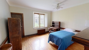 A room with a bed, a wooden desk, a radiator, a window, and a ceiling fan. - Knox Residence University of Toronto (Toronto)