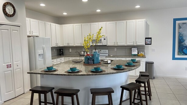 Una cocina moderna con armarios blancos, encimera de granito y una isla central con taburetes.