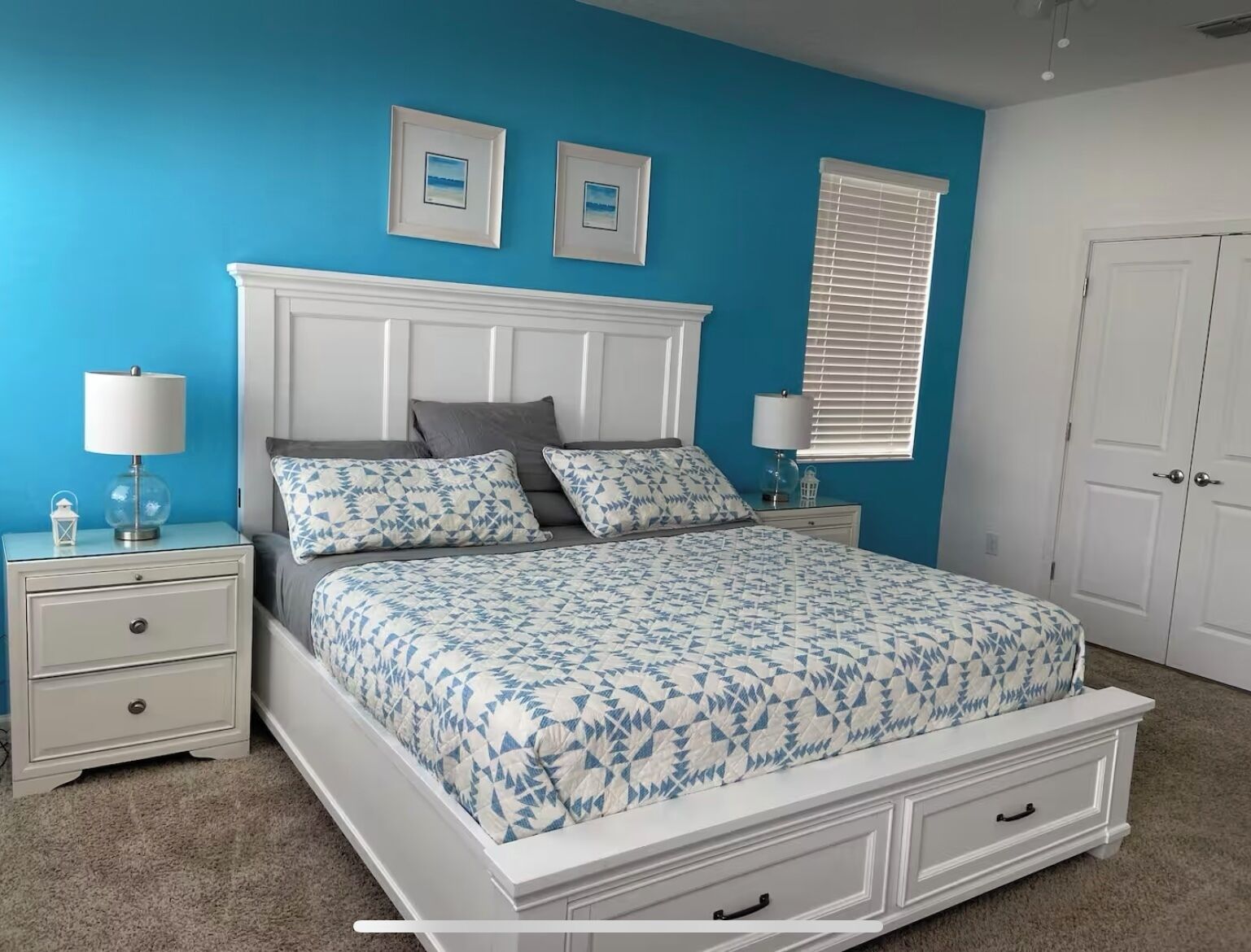 A bedroom with a bed, two bedside tables, a nightstand, a window with blinds, and a door.