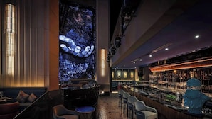 A bar area with a large digital screen displaying a blue abstract image, bar stools, and a variety of bottles on shelves. - Lovely Studio Burj Khalifa View (Dubai)