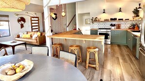 Une cuisine moderne dotée d’un îlot central, de tabourets en bois et d’une table à manger sur laquelle se trouve un saladier rempli de fruits.