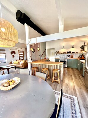 Una cucina moderna con isola centrale, sgabelli in legno e un tavolo da pranzo con una ciotola di frutta.