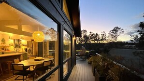 Une maison moderne dotée d’une terrasse en bois, de grandes fenêtres et d’un coin repas avec une table et des chaises.