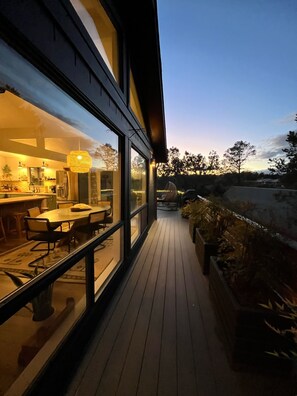 Una casa moderna con una terrazza in legno, ampie finestre e un'area pranzo con tavolo e sedie.
