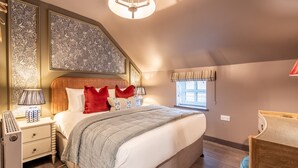 A bedroom with a large bed, a nightstand with a lamp, a window with curtains, and a ceiling light.