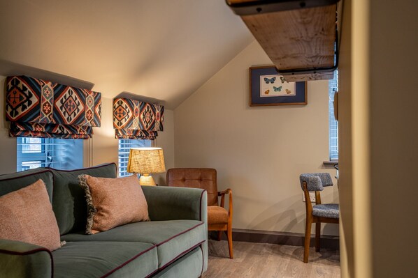A cozy living room with a green sofa, two chairs, patterned curtains, and a framed butterfly picture on the wall. - The Falcon - Apartment 3 -  a couples retreat that sleeps 2 guests  in 1 bedroom (York)