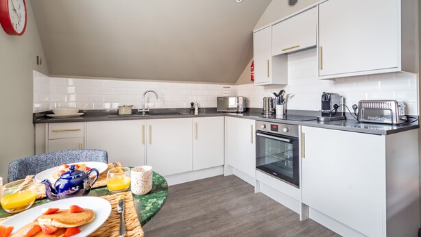 A modern kitchen with white cabinets, a black countertop, and a breakfast setup including pancakes, strawberries, and orange juice.