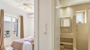 A modern bedroom with a bed, a bathroom with a shower, and a balcony with a table and chairs. - Ampelas | 3BR Cycladic House | White Heaven Apt4 (Ampelas)