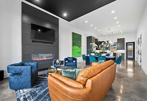 A modern living room with a fireplace, blue chairs, a leather sofa, and a dining area with teal chairs.