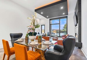 A modern dining area with a glass table, black and orange chairs, and a large window offering a view of the outdoors.
