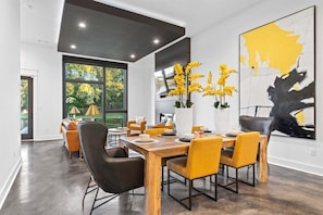 A modern dining area with a wooden table and chairs, a vase with yellow flowers, and a large abstract painting on the wall.