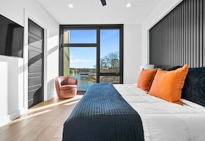 A modern bedroom with a large window, a bed, a bench, and a chair.