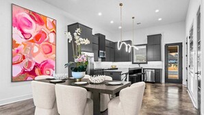 Una cocina moderna con muebles oscuros, un comedor con un cuadro abstracto grande y vistas al exterior.