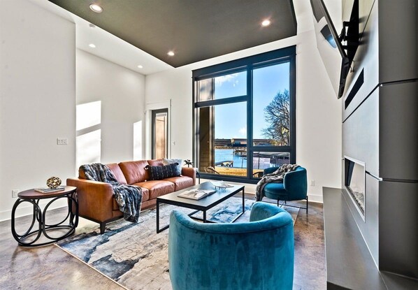 A modern living room with a sofa, coffee table, and chairs, a large window with a view, and a built-in fireplace.