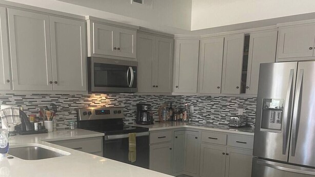 Una cocina moderna con gabinetes grises, una isla central, electrodomésticos de acero inoxidable y salpicadero de azulejos.