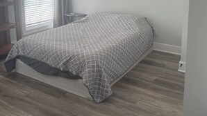 Un dormitorio con cama, ventilador de techo, ventana con persianas y suelo de madera.