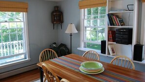 A dining area with a wooden table, chairs, a striped table runner, and a bookshelf with books and a radio. - Captain's Quarters Cottage at Dockside Guest Quarters in York Harbor,  Maine. (YORK)
