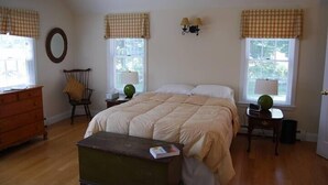 A bedroom with a large bed, two bedside tables with lamps, a dresser, a chair, and a mirror on the wall. - Captain's Quarters Cottage at Dockside Guest Quarters in York Harbor,  Maine. (YORK)