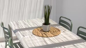 A table with a woven placemat and a potted plant, set against a white wall with vertical lines. - Naousa | 2BR Cycladic Town-House | Jasper (Naousa)