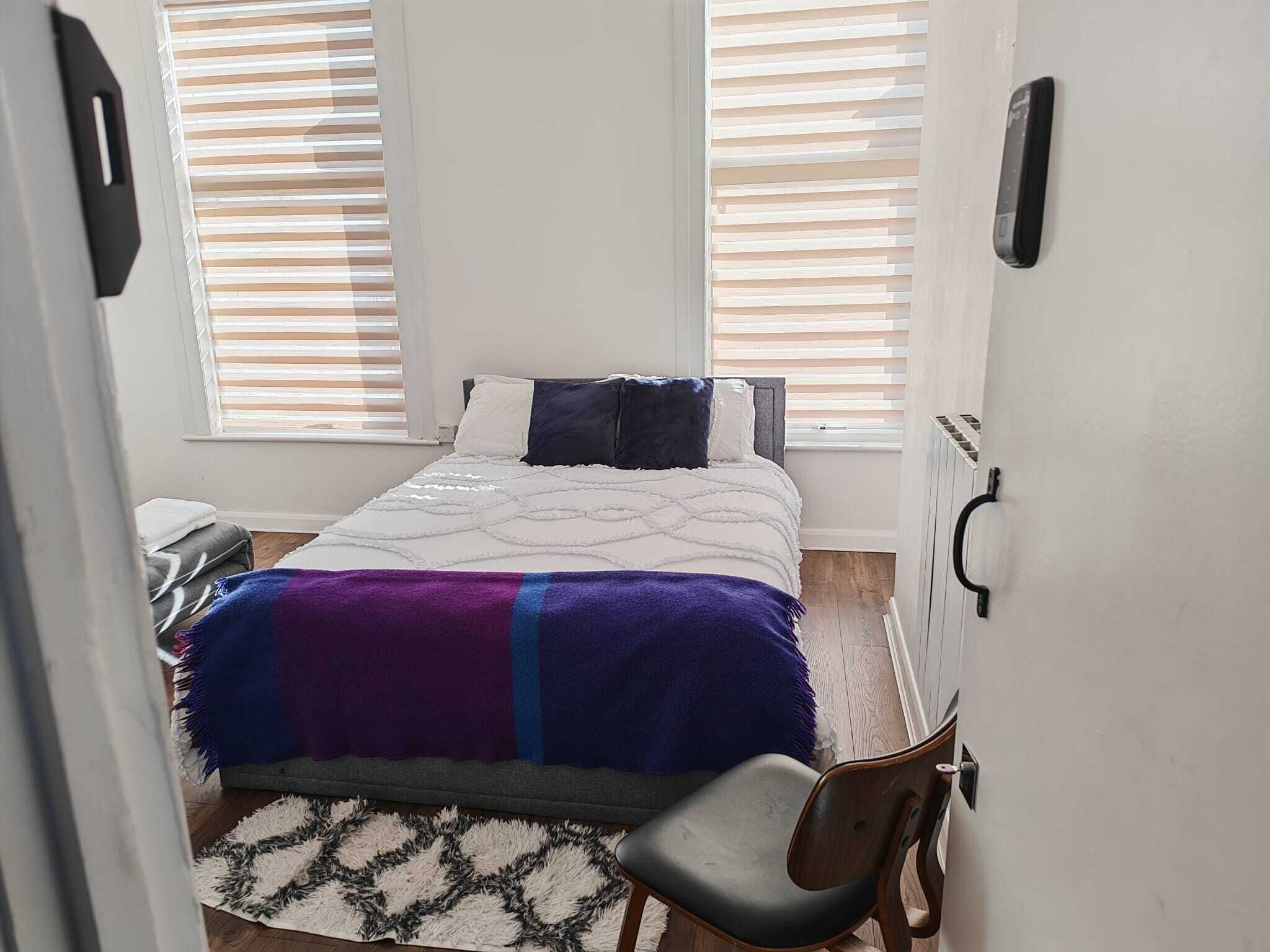 Ein Schlafzimmer mit Bett, Stuhl, Schreibtisch und einem Fenster mit Jalousien.