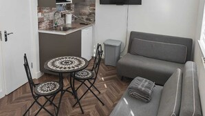 A compact living space with a kitchenette, a dining table with chairs, a grey sofa, and a flat-screen TV mounted on the wall. - Dalston Luxe Studios (3 Miles away from Liverpool Train Station) (London)