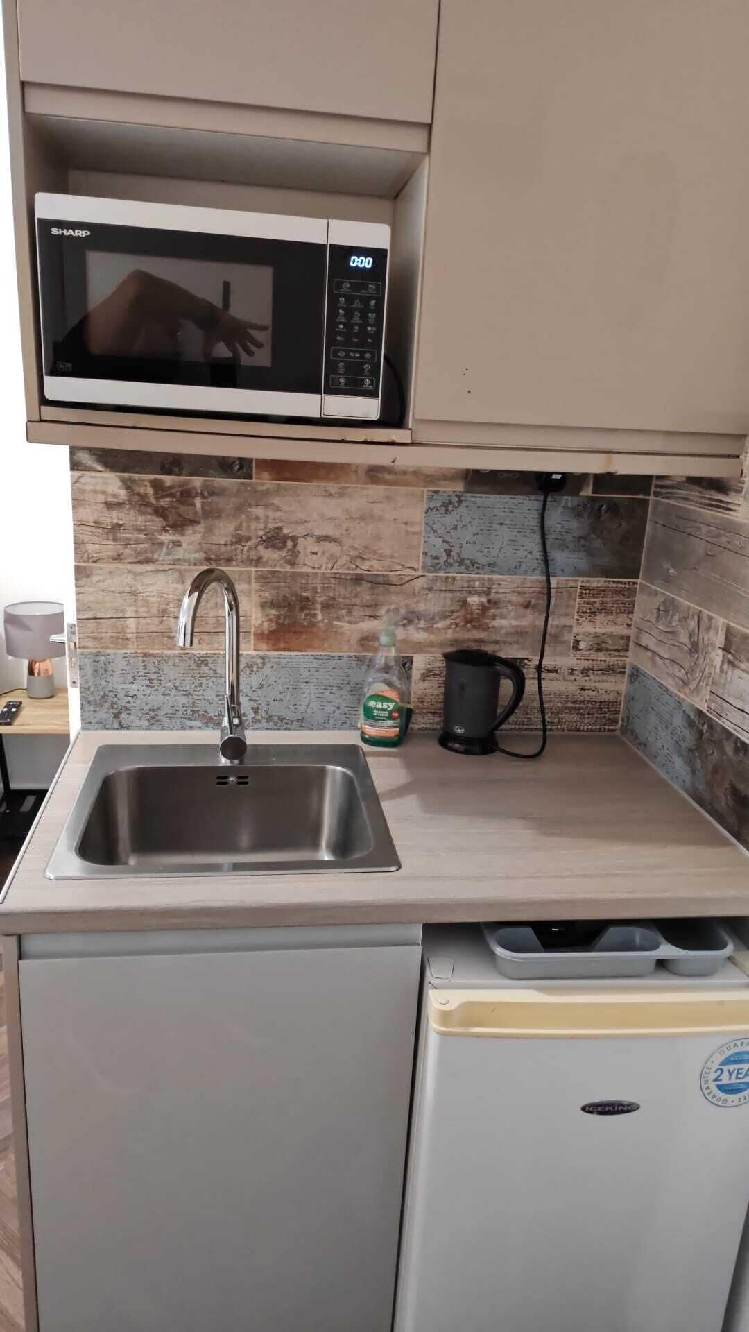 A kitchen with a stainless steel sink, a microwave, a kettle, and a dishwasher.