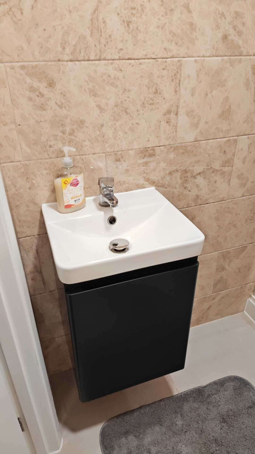 A bathroom with a white sink, a black cabinet below, and beige tiled walls.