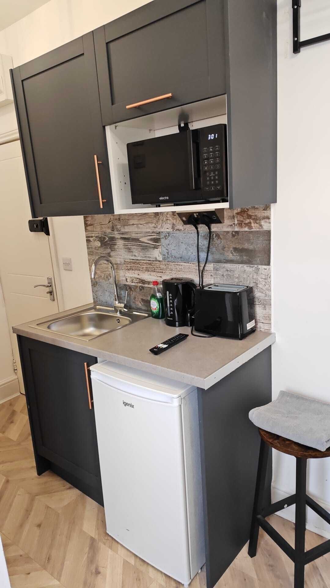 Una cocina compacta con microondas, cafetera y un refrigerador pequeño.