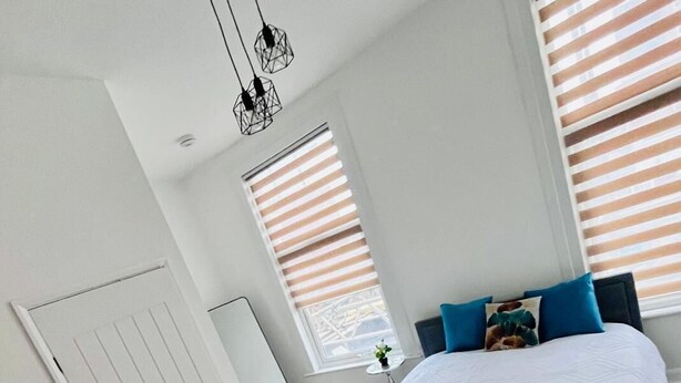 A modern bedroom with a bed, bedside table, and a window with blinds. - Dalston Luxe Studios (3 Miles away from Liverpool Train Station) (London)