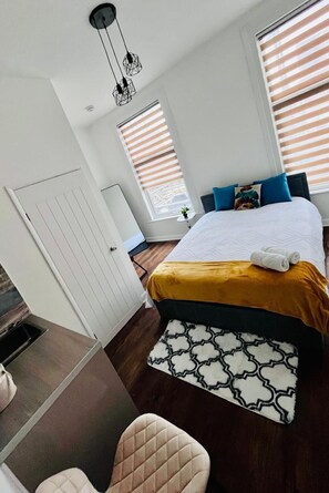 A modern bedroom with a bed, bedside table, and a window with blinds. - Dalston Luxe Studios (3 Miles away from Liverpool Train Station) (London)
