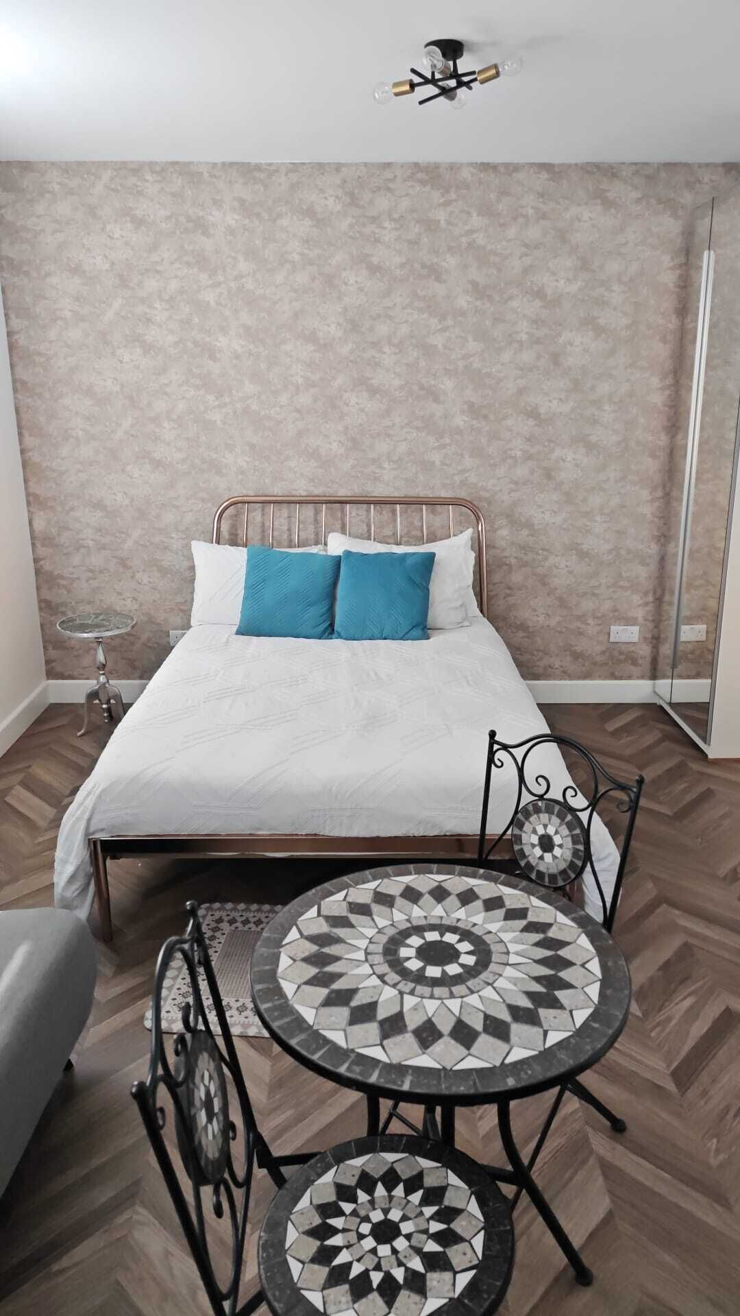 Une chambre à coucher comprenant un lit, deux tables de chevet, une table ronde avec des chaises et un luminaire suspendu.