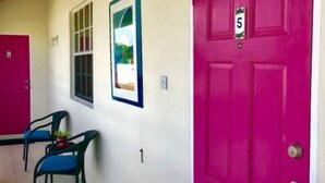 Una habitación con una puerta rosa brillante marcada con el número 5, una ventana con vistas y dos sillas azules.