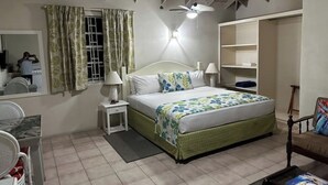 Un dormitorio con cama, mesitas de noche, ventilador de techo, ventana con cortinas, espejo y una silla.