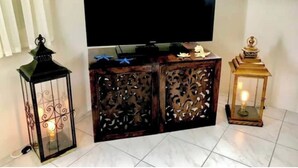 A TV on a wooden cabinet with intricate carvings, flanked by two lit lanterns. - Villa Mia 2bed Apartment # 3 (Oistins)