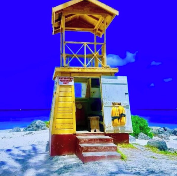 Una torre de salvavidas con un cartel que indica que es solo para personal autorizado, ubicada en una playa con rocas y un cielo azul despejado.