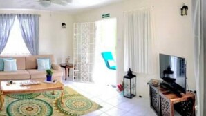 A living room with a beige sofa, a coffee table, and a TV stand. - Villa Mia 2bed Apartment # 3 (Oistins)