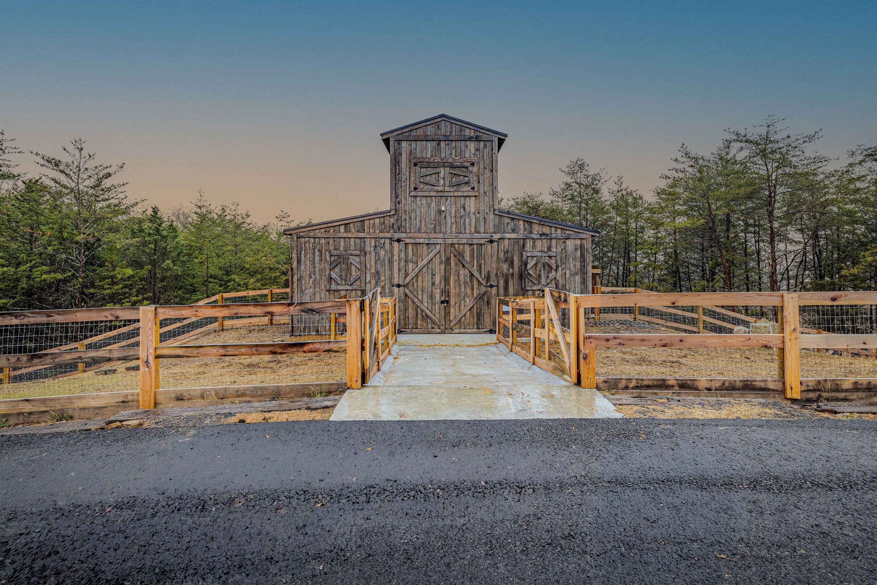 A rustic wooden barn with a metal gate and a concrete pathway leading to it.
